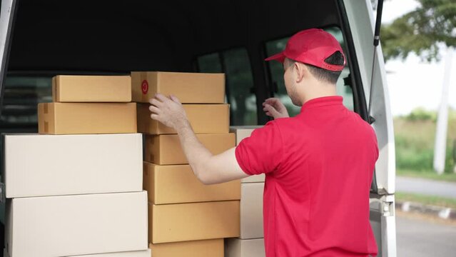Handsome Asian man holding a cardboard parcel box standing in front of a house with a van in the background, delivery concept. 4K resolution.