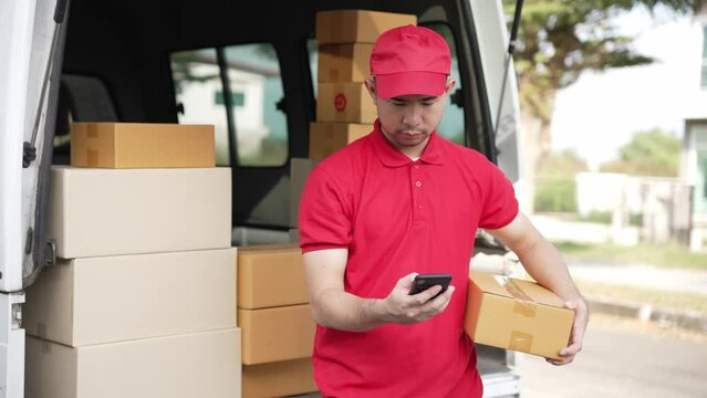 Handsome Asian man holding a cardboard parcel box standing in front of a house with a van in the background, delivery concept. 4K resolution.