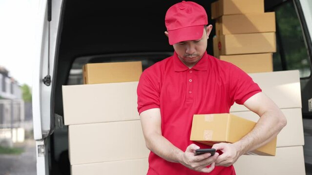 Handsome Asian man holding a cardboard parcel box standing in front of a house with a van in the background, delivery concept. 4K resolution.