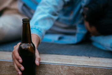 Focus on beer bottle, Asian sleepy drunk man holding beer bottle and lying on floor after nightlife...
