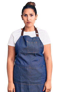 Young beautiful brunette woman wearing apron with serious expression on face. simple and natural looking at the camera.
