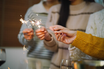 Cheerful friends enjoying home Birthday holiday party. Asian Friends hold lights with sparkling Sparkler celebrating Christmas or New Year eve party.
