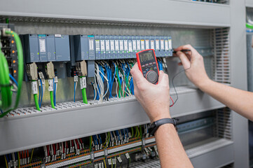 Electrician checks voltage in PLC card with meassuring instrument in electrical cabinet