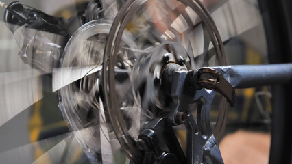 Close-up of a mountain bike cassette with chain, brake disc with caliper and wheel spokes. The spinning makes the image blurred. Repair and maintenance of a bicycle in a specialised workshop.