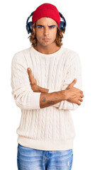 Young hispanic man listening to music using headphones skeptic and nervous, disapproving expression on face with crossed arms. negative person.