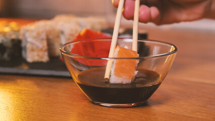 Sushi roll dipped in soy sauce with sushi chopsticks close up. Sushi is a Japanese dish eaten in a...
