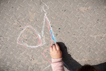 On a sunny spring day, a little girl in the city square draws patterns on the asphalt path with...