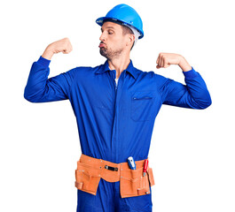 Young handsome man wearing worker uniform and hardhat showing arms muscles smiling proud. fitness concept.
