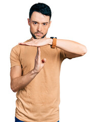 Hispanic man with beard wearing casual t shirt doing time out gesture with hands, frustrated and...