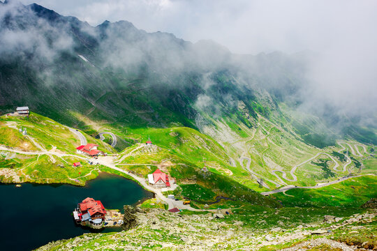 landscape of high altitude mountain lake in summer. nature scenery of valley with transfagarasan road in the distance beneath a sky with clouds on a sunny day. popular travel destination of romania