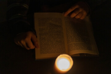 A child reads a book by candlelight. Power outage due to war in Ukraine