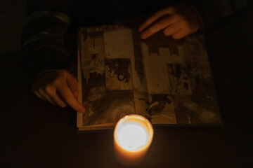 A child reads a book by candlelight. Power outage due to war in Ukraine