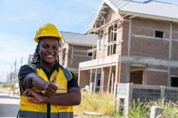 Black woman in yellow uniform and helmet for safety, happy working, service, thumbs up, ready to provide house construction on construction project, site, land development.