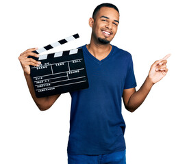 Young african american man holding video film clapboard smiling happy pointing with hand and finger...