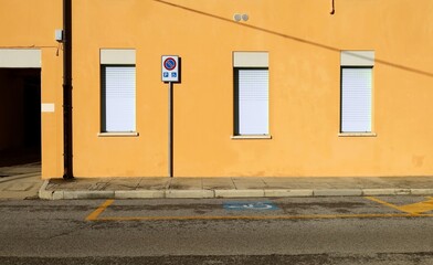 No stopping and disabled parking sign only, on concrete sidewalk with yellow facade with row of shutters on behind. Urban street in front, Background for copy space.
