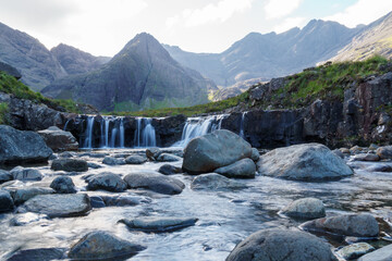 Fairy pool waterfalls and distant mountains in the Isle of Sky. A series of rocks is spread across the pool.