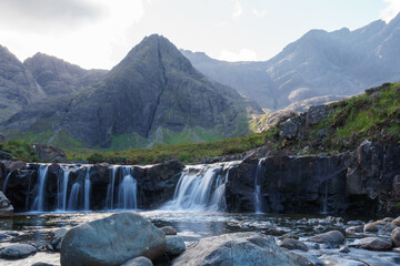 Fototapeta na wymiar Fairy pool waterfalls and distant mountains in the Isle of Sky. Blurred water and foreground boulder.
