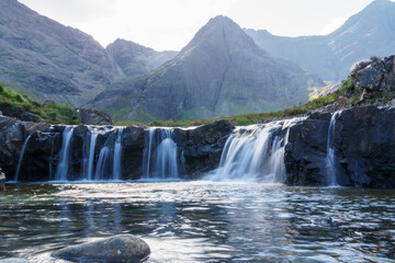 Fototapeta na wymiar Fairy pool waterfalls and distant mountains in the Isle of Sky. Blurred water and lone foreground rock.