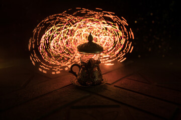 Arabian tea in glass with eastern snacks on a carpet on dark background with lights and smoke....