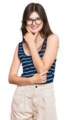 Young beautiful caucasian girl wearing casual clothes and glasses looking confident at the camera smiling with crossed arms and hand raised on chin. thinking positive.