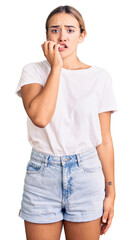 Young beautiful blonde woman wearing casual white tshirt looking stressed and nervous with hands on...