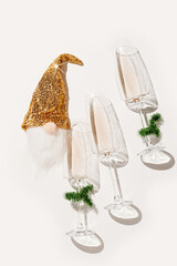 Minimal New Year flat lay with white wine in champagne glasses, Christmas green tinsel, golden gnome toy for bottle decor. Holiday aesthetic still life photo, top view wineglass, sunlight, star