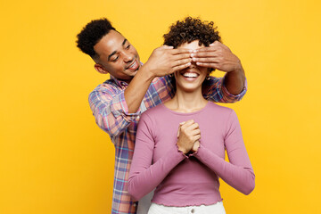 Young couple two friend family man woman of African American ethnicity wear purple casual clothes together close eyes with hands play guess who or hide and seek isolated on plain yellow background.
