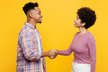 Young couple two friends family man woman of African American ethnicity wear casual clothes together hold hands folded handshake gesture isolated on plain yellow background. Friendship greet concept.