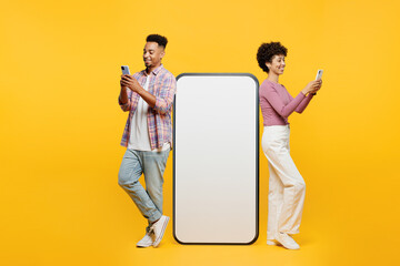 Full body side view young couple two friend family man woman wear purple casual clothes together big huge blank screen mobile cell phone with area using smartphone isolated on plain yellow background - obrazy, fototapety, plakaty