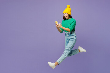 Full body young woman she wear green sweater yellow hat casual clothes jump high hold in hand use...