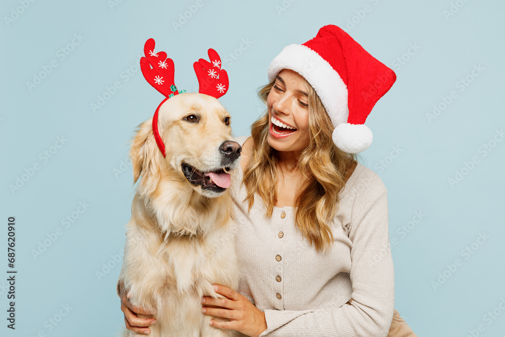 Poster Young smiling owner woman wear casual clothes Santa hat hug cuddle embrace best friend pet retriever dog isolated on plain pastel light blue background studio. New Year Christmas celebration concept.