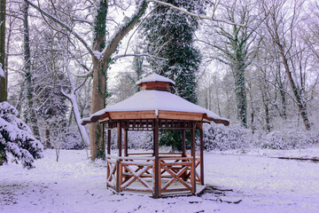 Drewniana altana w stylu japońskim w parku w Iłowej. Jest zima. Dach altany, pobliskie drzewa i ziemię pokrywa warstwa śniegu. - obrazy, fototapety, plakaty