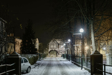 Ulica Pałacowa w miejscowości Iłowa w Polsce. Jest zimowa noc, jezdnię i chodnik pokrywa...