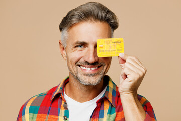 Close up adult man he wear red shirt white t-shirt casual clothes cover eye with mock up of credit bank card isolated on plain pastel light beige color background studio portrait. Lifestyle concept.