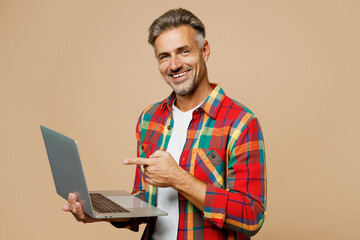 Adult IT man wear red shirt white t-shirt casual clothes hold use work point index finger on laptop pc computer isolated on plain pastel light beige color background studio portrait Lifestyle concept