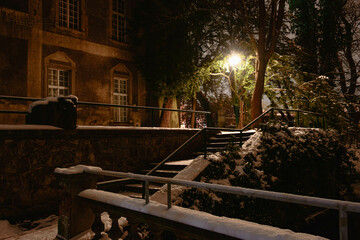 Park dworski w Iłowej nocą. Wśród ciemności widać krużganki, schody, kładki znajdujące się przy budynku pałacu.