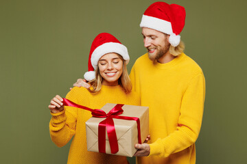 Merry young couple two friend man woman in sweater Santa hat posing hold open present box with gift ribbon bow isolated on plain green background Happy New Year celebration Christmas holiday concept
