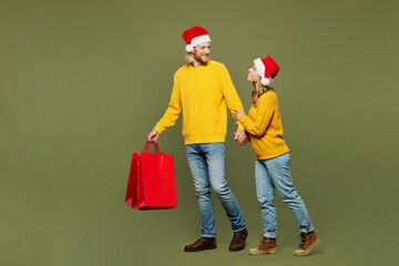 Full body sideways merry young couple two friends man woman wears sweater Santa hat posing hold...