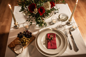 holidays, romantic date and celebration concept - close up of festive table serving for two with flowers in vase and candles burning at home on valentine's day