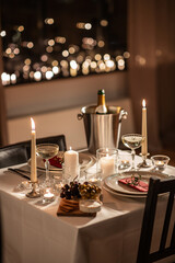 holidays, romantic date and celebration concept - close up of festive table serving for two with champagne bottle in ice bucket and candles burning at home on valentine's day