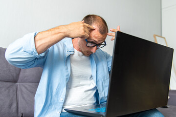 European man having stress about his hair loss problem sitting at home with a laptop. Baldness is related to your genes and male sex hormones. Online medical consultations, telemedicine concept - obrazy, fototapety, plakaty