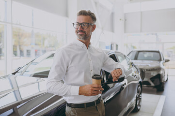 Naklejka na ściany i meble Adult man customer buyer client wear shirt hold takeaway delivery cup coffee to go loot at watch choose auto wants buy new automobile in car showroom salon dealership store motor show. Sales concept.
