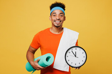 Young fitness trainer instructor sporty man sportsman wear orange t-shirt hold caremat towel clock...