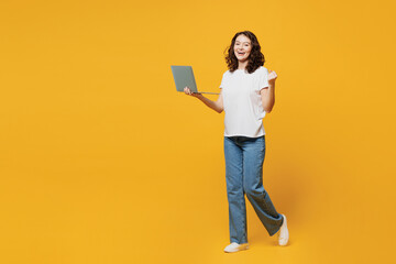 Full body young IT woman wear white blank t-shirt casual clothes hold use work on laptop pc computer do winner gesture go isolated on plain yellow orange background studio portrait. Lifestyle concept.