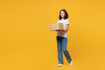 Full body side view young happy courier woman she wears white blank t-shirt casual clothes hold cardboard box look camera isolated on plain yellow orange background studio portrait. Lifestyle concept.
