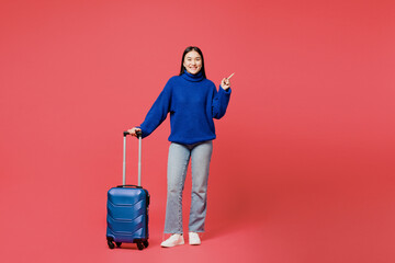 Traveler woman wearing blue sweater casual clothes hold suitcase point aside isolated on plain pink...