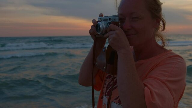 Inspired photographer takes pictures of beautiful landscape at sunset on retro film camera in travel.