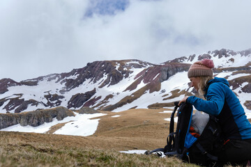 Traveling woman with bag sitting on hunches by snowy mountain