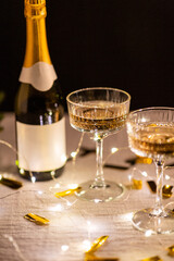 party, celebration and holidays concept - close up of champagne in glasses, electric garland lights and golden confetti on table over black background