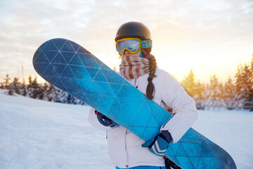 Portrait Of Woman On The Background Of Mountains and Sunset. Holding a Snowboard And Wearing Ski...